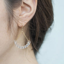Handmade glass arc pieces resembling gathered water droplets, suspended at both ends by twin gold‑plated chains from a hook.