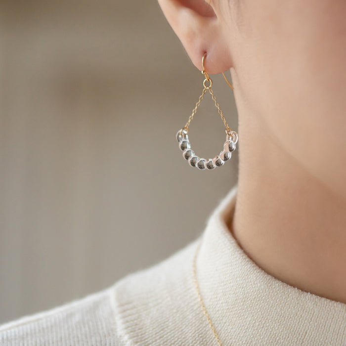 Handmade glass arc pieces resembling gathered water droplets, suspended at both ends by twin gold‑plated chains from a hook.