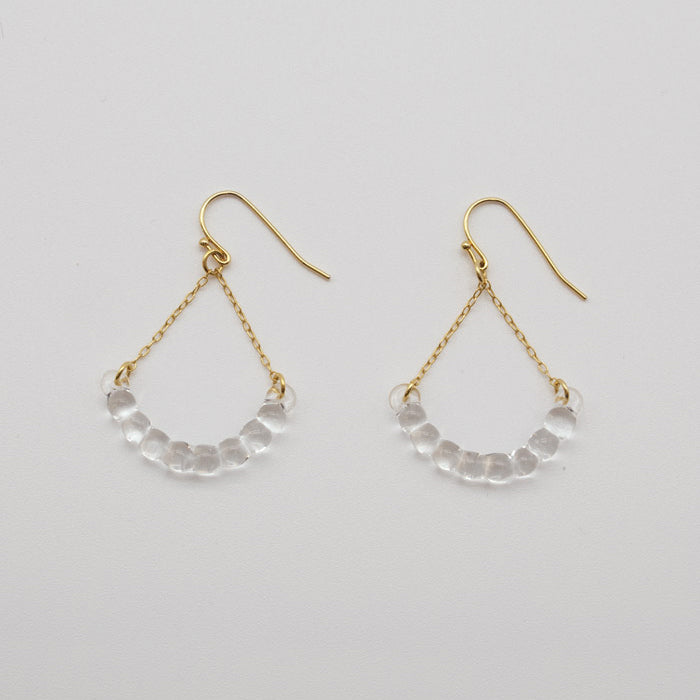 Handmade glass arc pieces resembling gathered water droplets, suspended at both ends by twin gold‑plated chains from a hook.